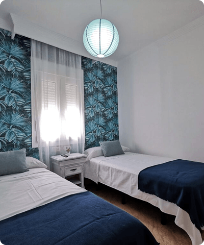 Habitación de hotel con al menos dos camas individuales, decoradas con manta y cojines de color azul